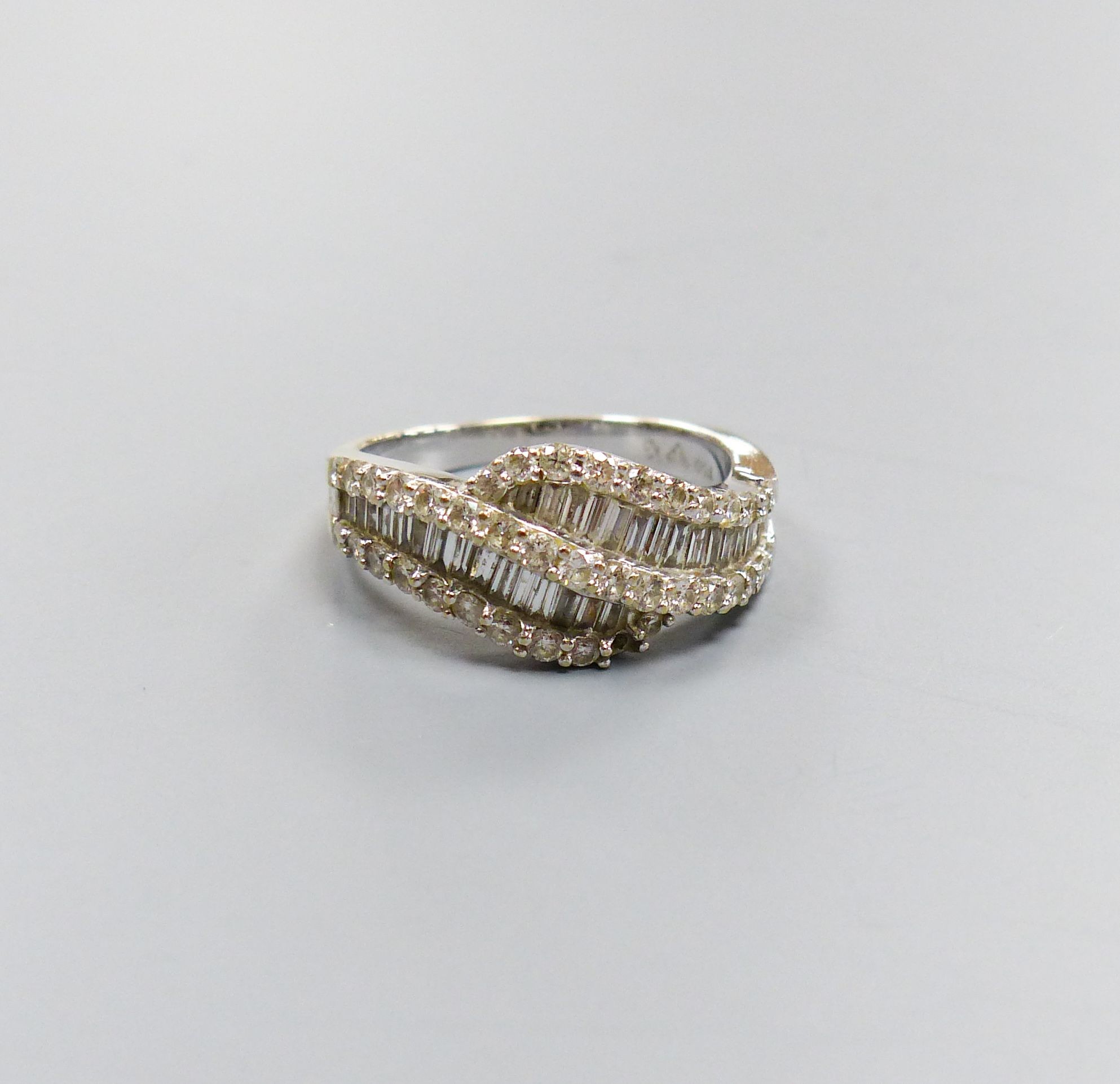 A modern 750 white metal, baguette and round cut diamond set two row crossover ring, size M/N, gross 5.4 grams, (one stone missing).